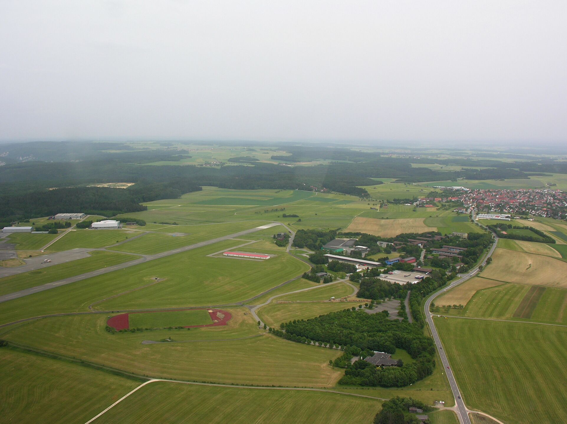 An aerial view of a rural landscape with fields, a small village, and a few buildings.