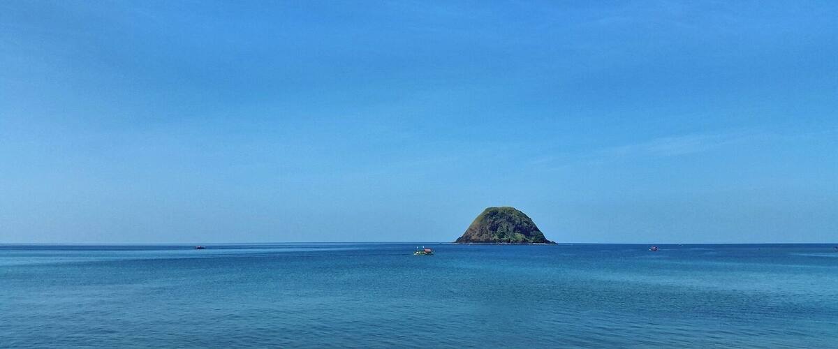 A clear blue sea with a small island in the distance.