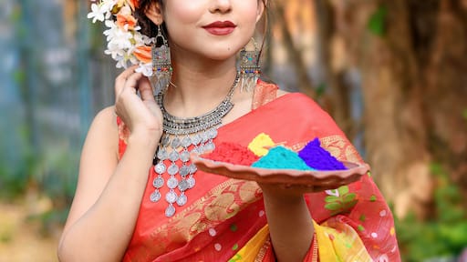 Portrait of pretty young indian girl wearing traditional saree and jewellery, holding powder colours in plate on the festival of colours called Holi, a popular hindu festival celebrated across india.