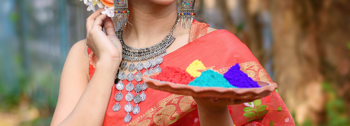 Portrait of pretty young indian girl wearing traditional saree and jewellery, holding powder colours in plate on the festival of colours called Holi, a popular hindu festival celebrated across india.