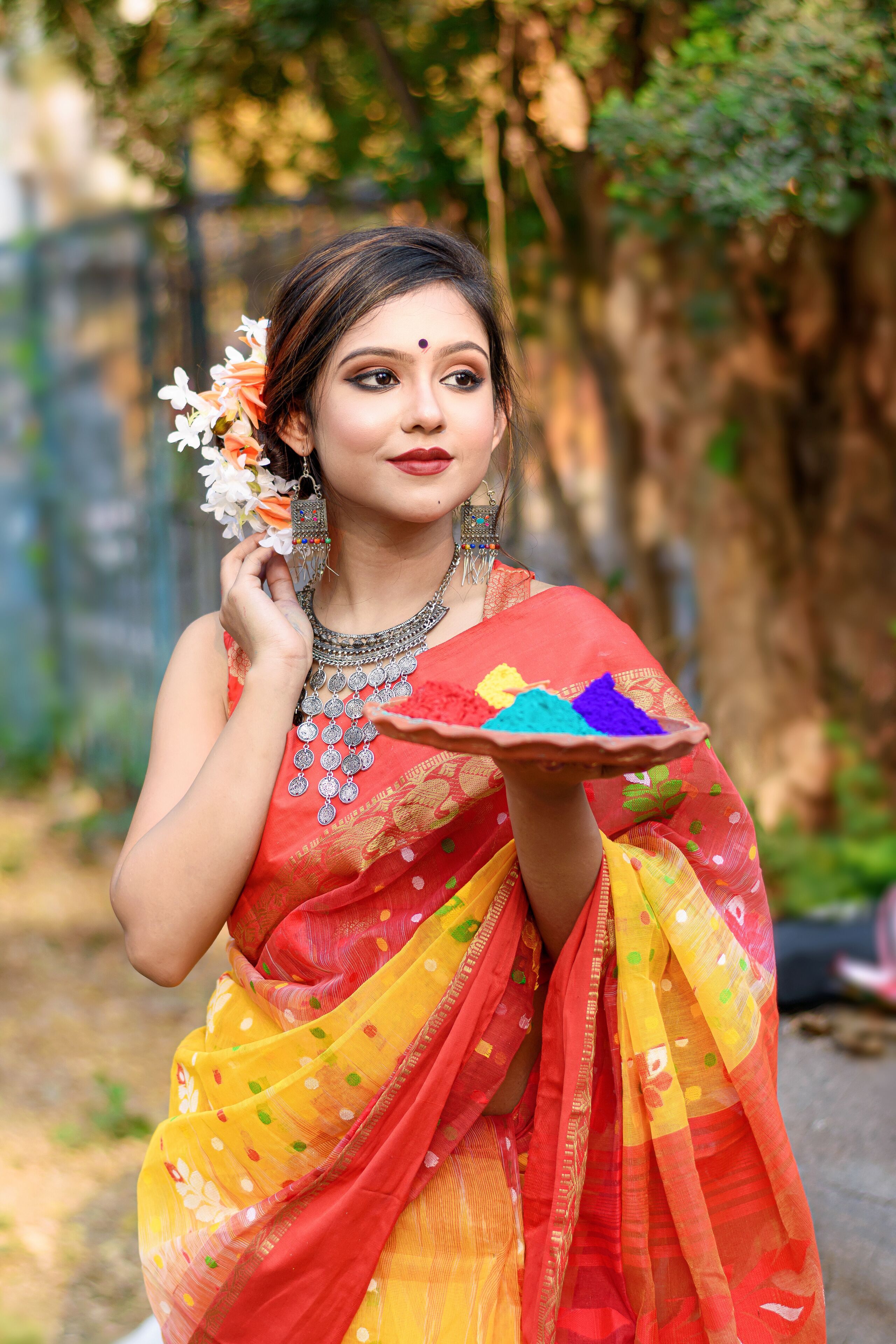 A person in a colorful saree holding a plate with colored powders.