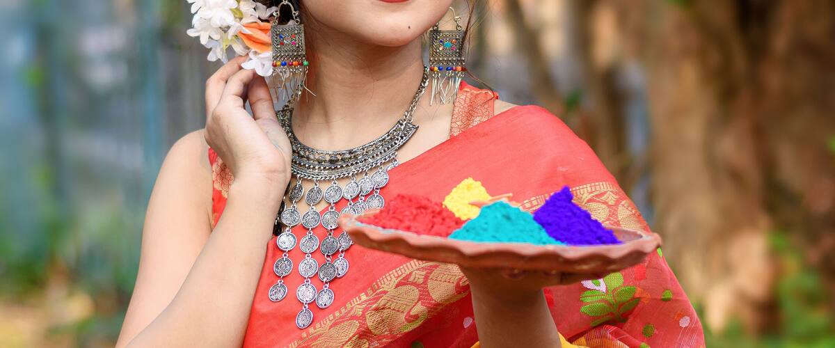 Portrait of pretty young indian girl wearing traditional saree and jewellery, holding powder colours in plate on the festival of colours called Holi, a popular hindu festival celebrated across india.