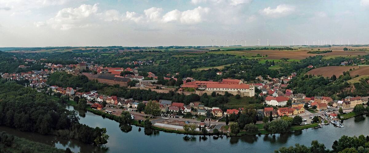 A town by a river with wind turbines in the distance.