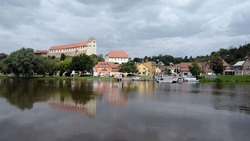 Ein ruhiger Fluss, der Gebäude, ein Schloss und ein am Ufer liegendes Boot spiegelt.