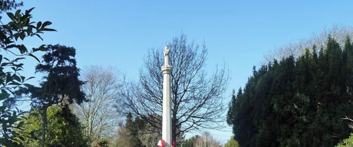A monument with a statue on top, surrounded by grass and trees.