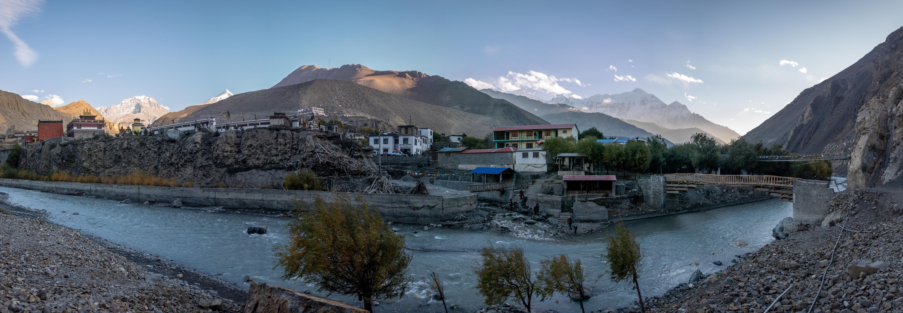 A river flowing through a mountainous village with buildings and a bridge.
