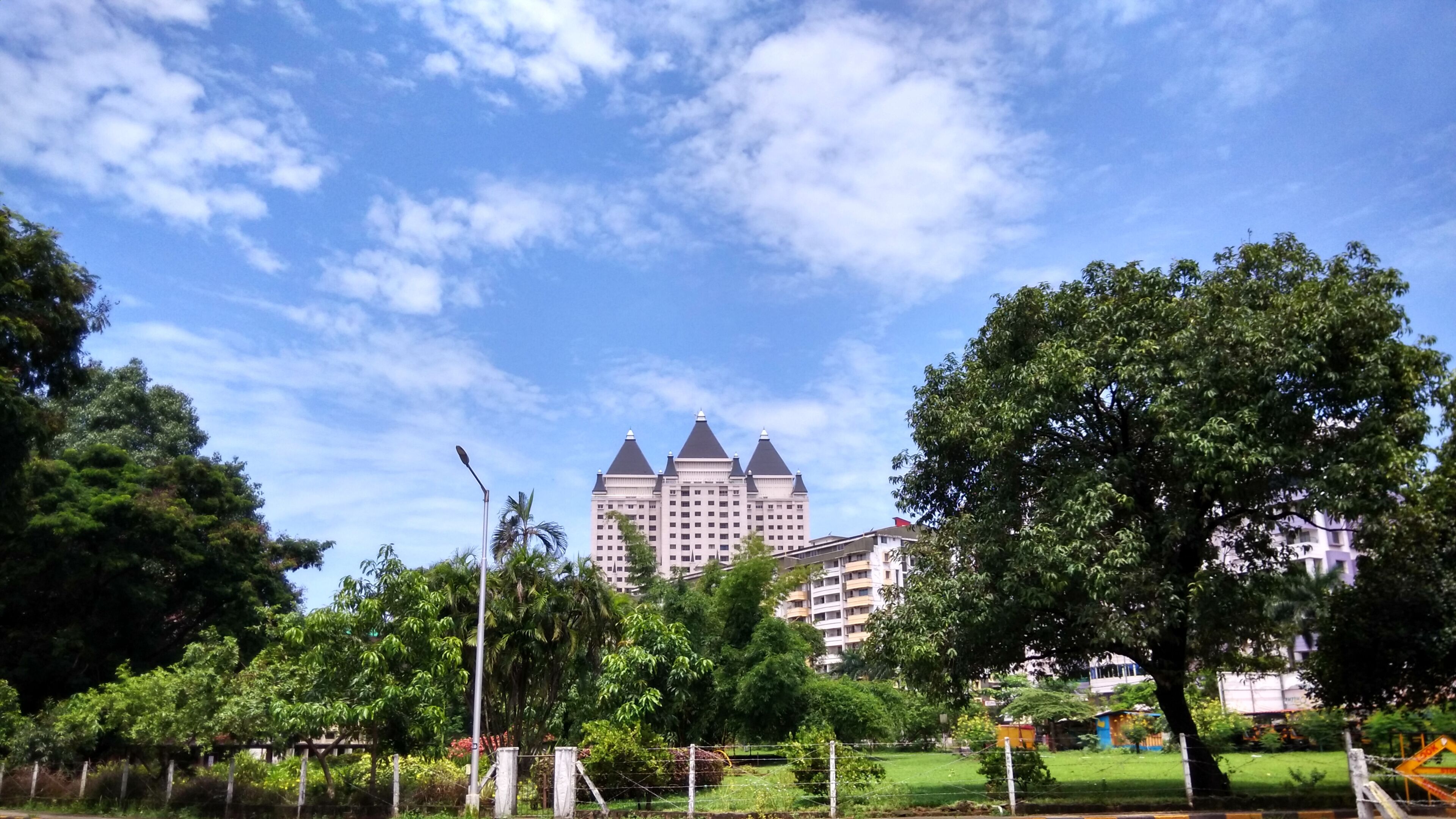 A large building with a distinctive architectural style, surrounded by lush green trees and a clear blue sky.