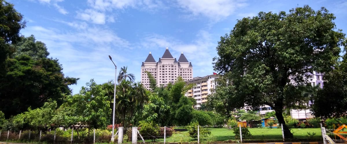 A large building with a distinctive architectural style, surrounded by lush green trees and a clear blue sky.