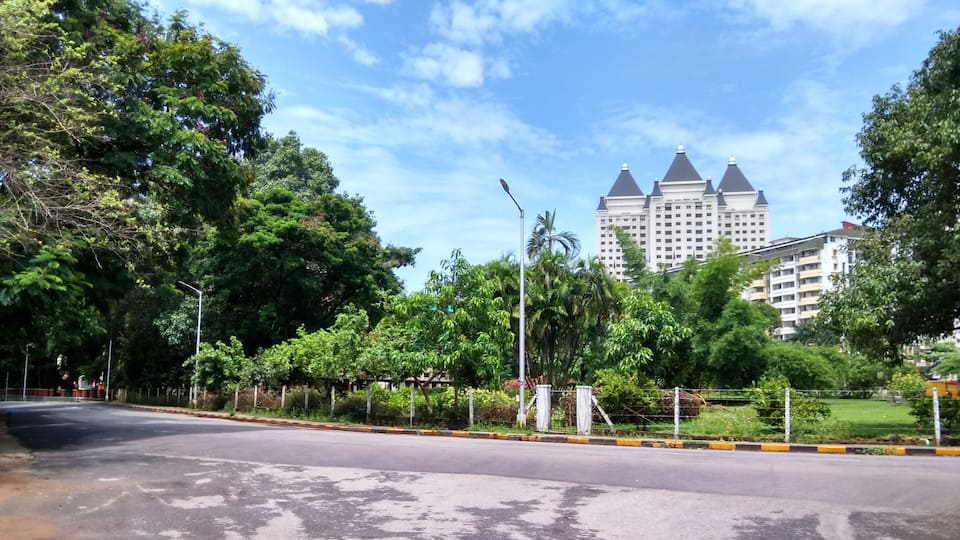 A road lined with trees and a large building with multiple towers in the background.