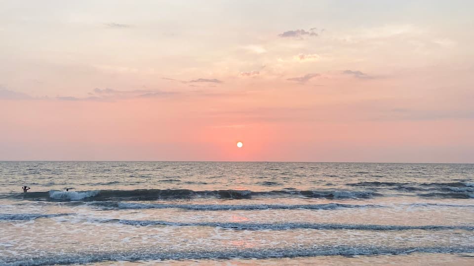 A beach with waves, rocks, and a sunset.