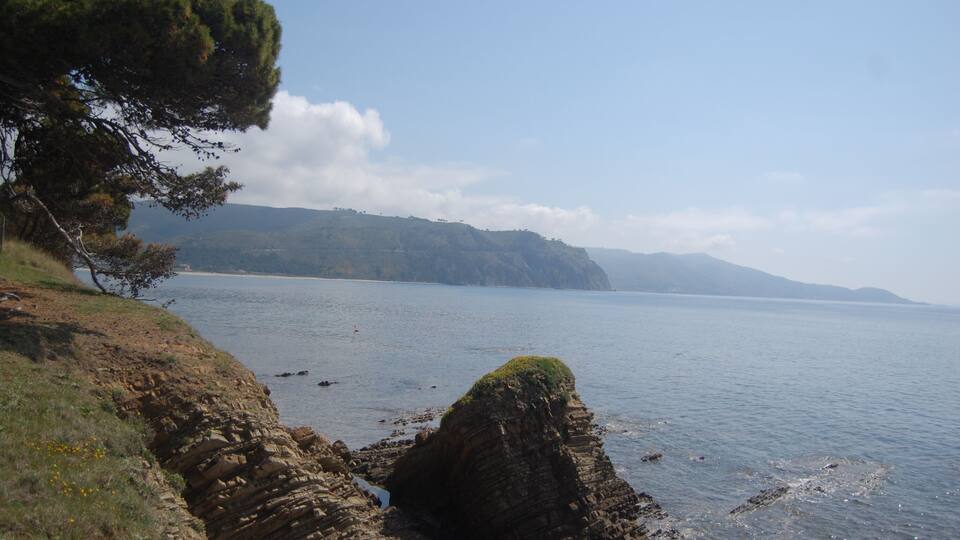 A coastal landscape with rocky cliffs, a clear sky, and distant mountains.