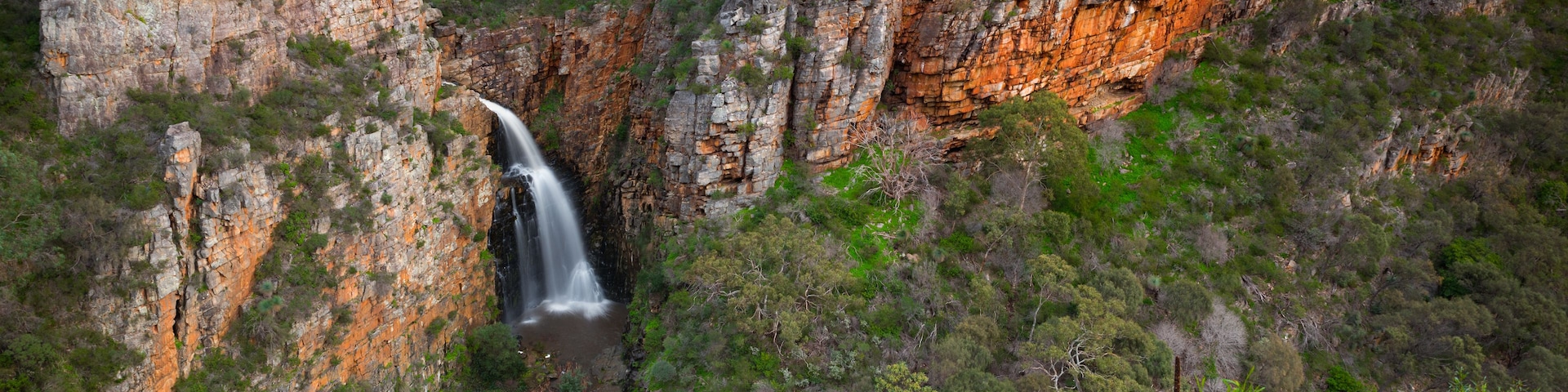 Ein Wasserfall stürzt über eine felsige Klippe, umgeben von dichtem Grün.