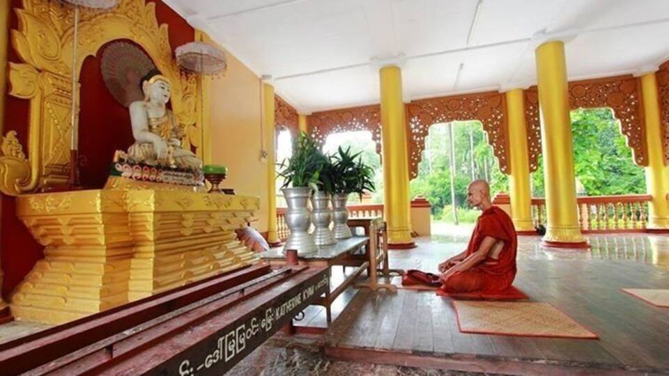 A monk meditating in a temple with golden statues and pillars.