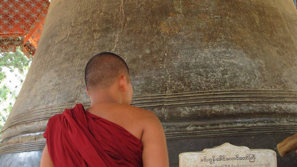 A monk in red robes standing before a large bell with inscriptions.