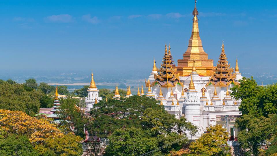 A large white temple complex with golden spires, surrounded by lush greenery.