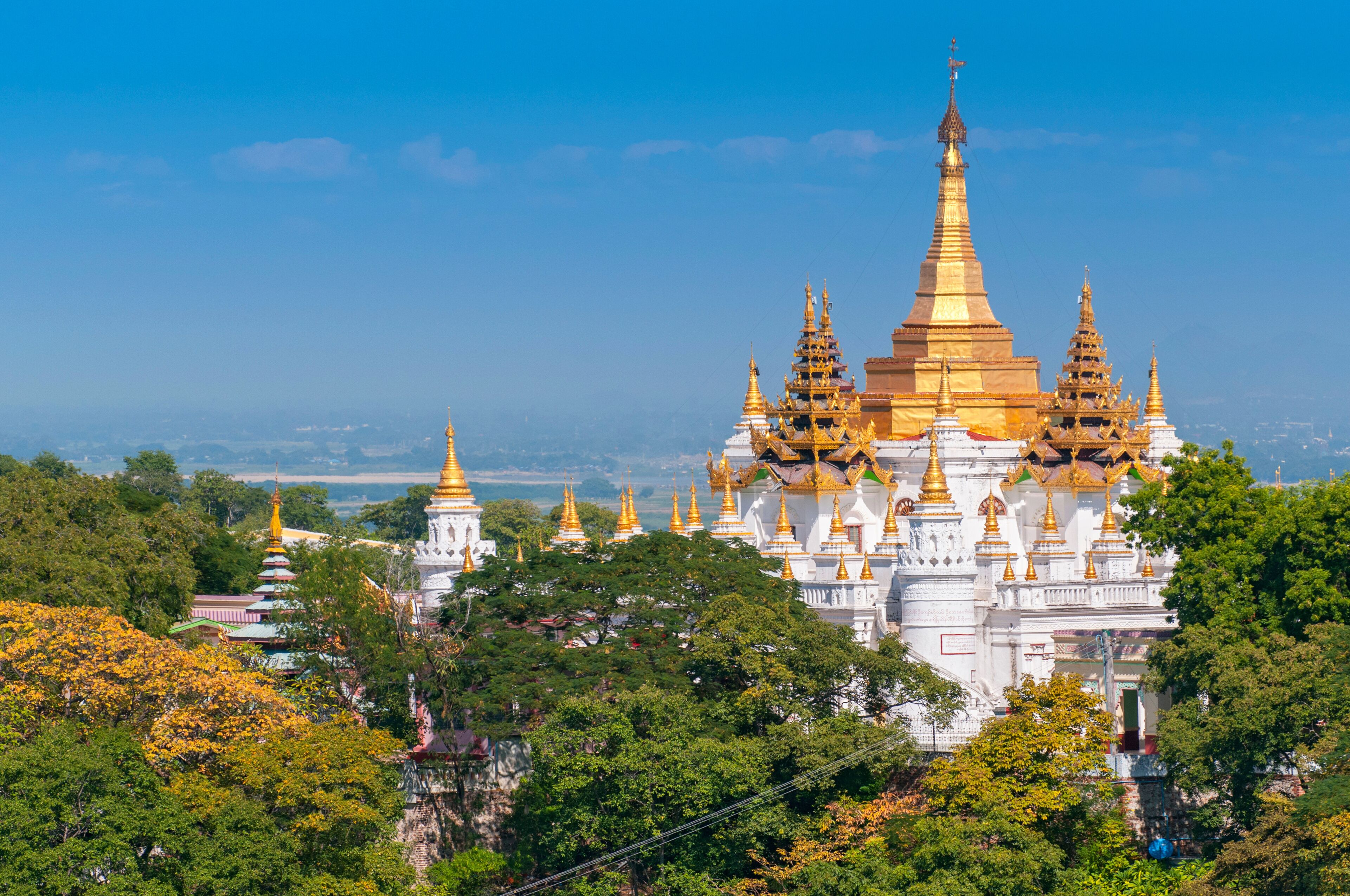 A large white temple complex with golden spires, surrounded by lush greenery.