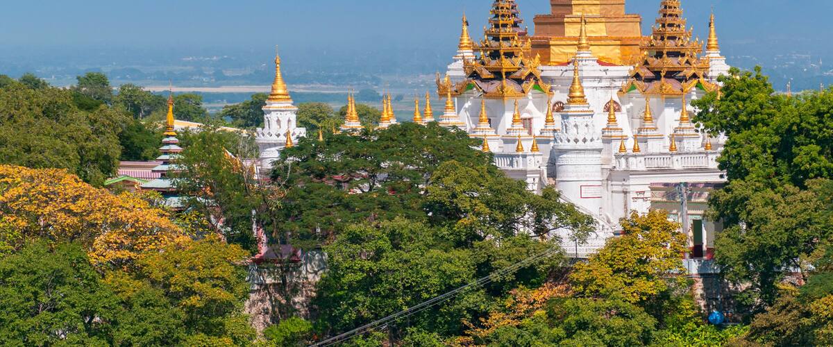 A large white temple complex with golden spires, surrounded by lush greenery.