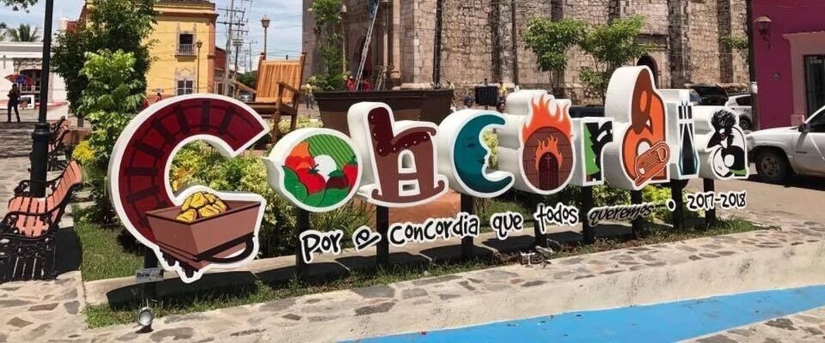 A street sign with 'Cochon' and 'Por Concordia que todos venemos' text, a historic building, and a clear blue sky.