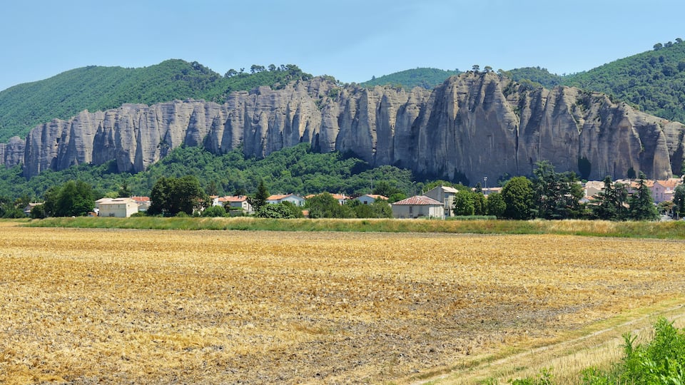 A rural landscape with a large limestone cliff, a field, and scattered houses.