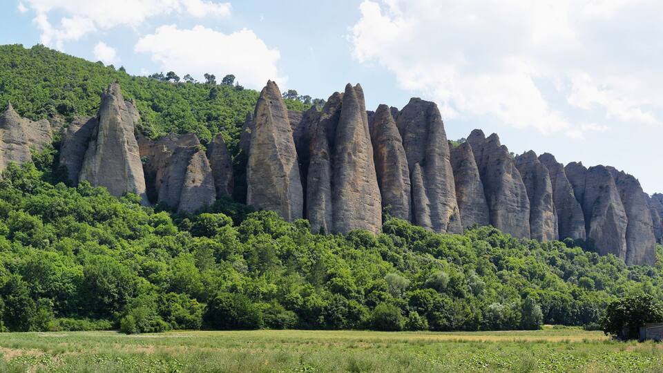 A landscape with tall, narrow rock formations and a lush green hill in the background.