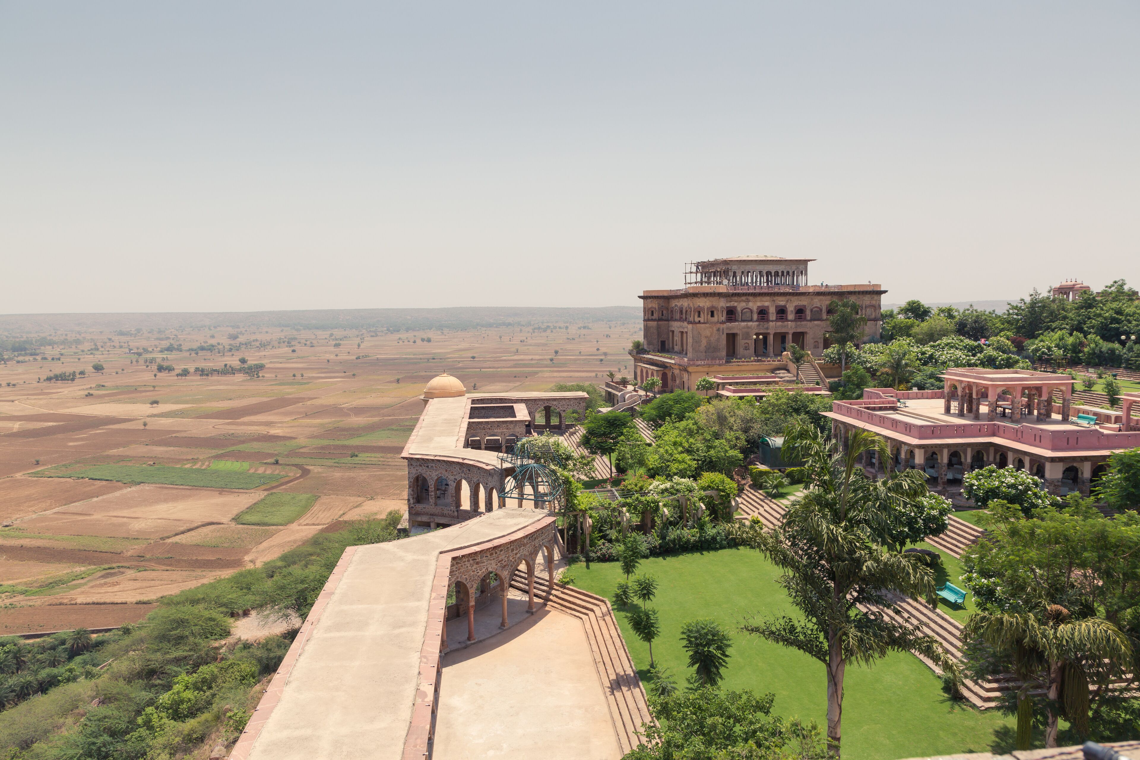 A historical building complex with arched structures and a large dome, surrounded by lush greenery and terraced fields.