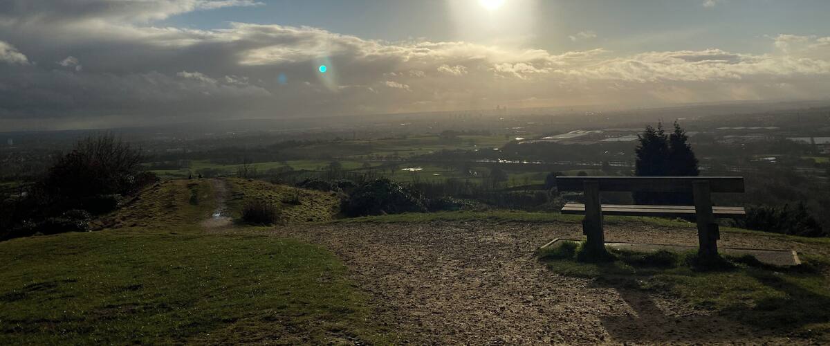 A bench overlooking a landscape with a sun shining through clouds.