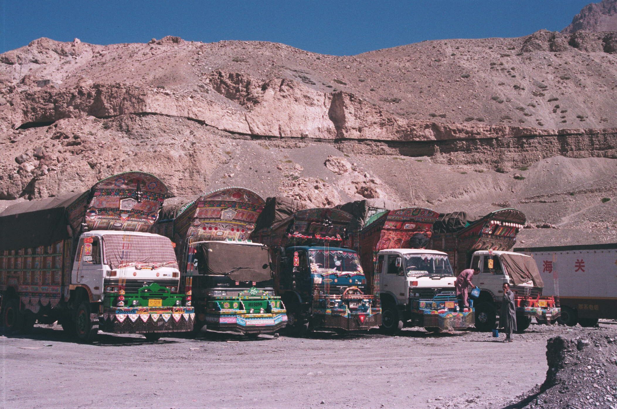 A row of colorful trucks parked in a desert with rocky hills in the background.
