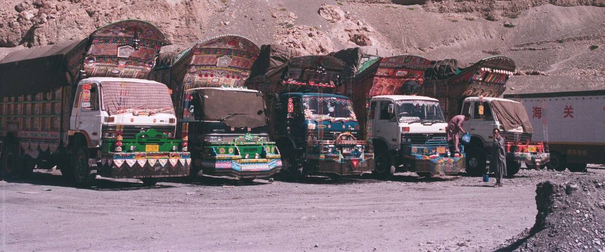 A row of colorful trucks parked in a desert with rocky hills in the background.