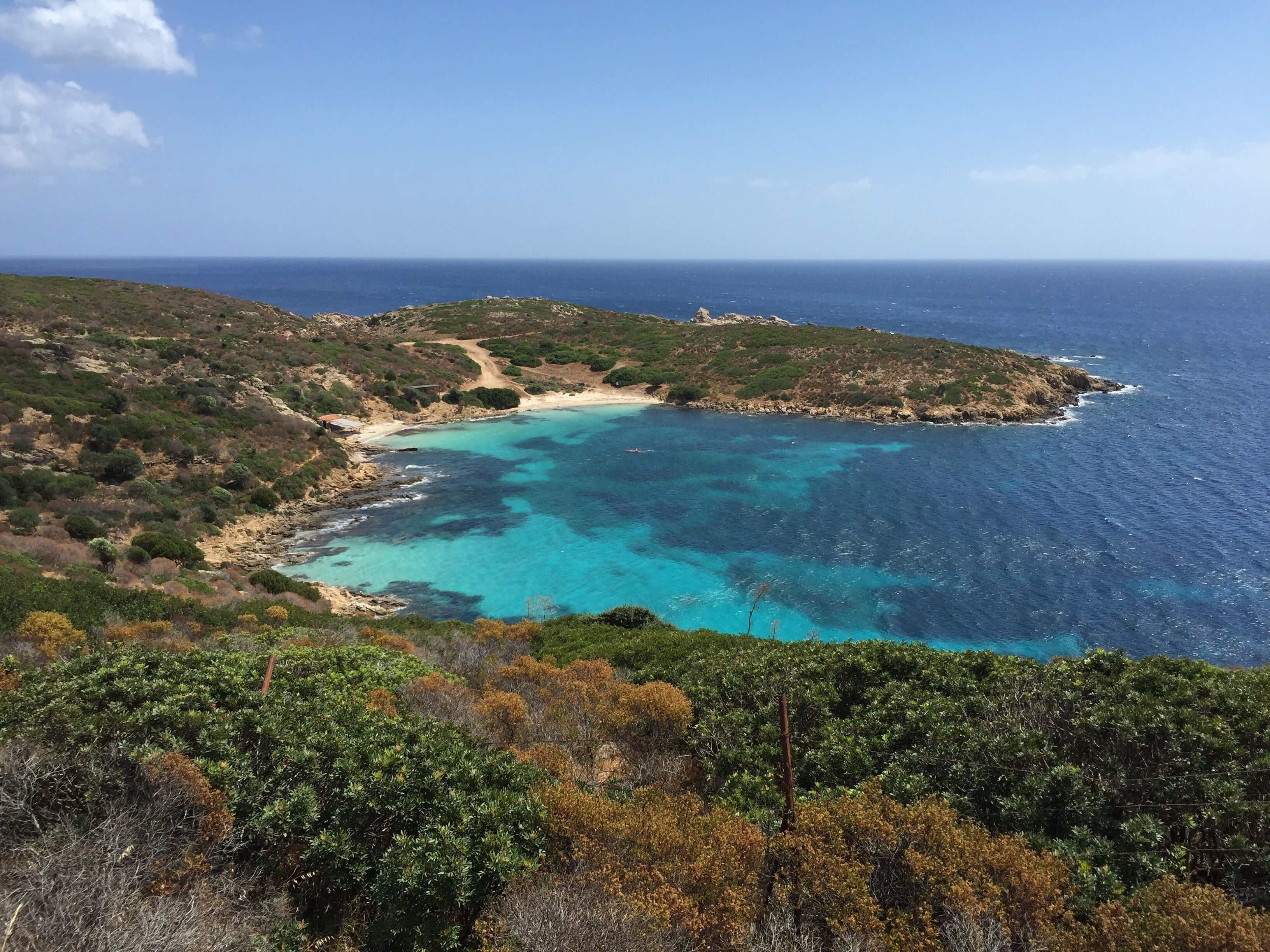 A coastal landscape with a turquoise bay, rocky cliffs, and dense vegetation.