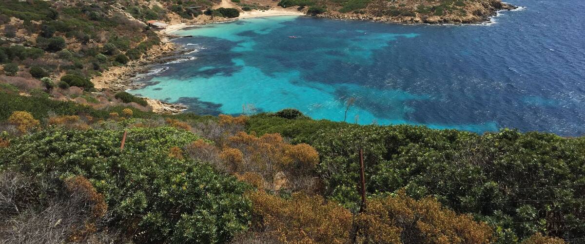 A coastal landscape with a turquoise bay, rocky cliffs, and dense vegetation.