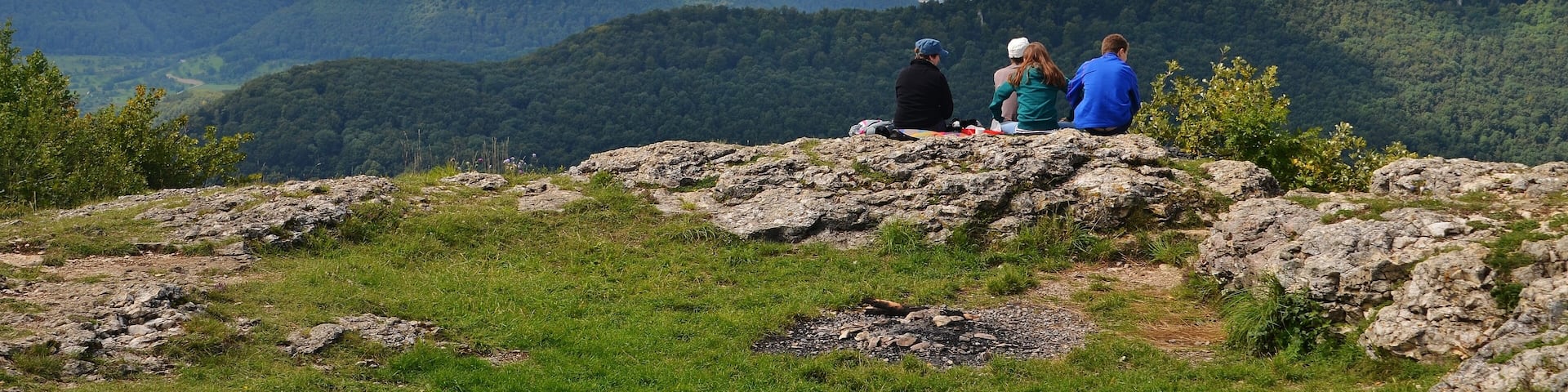 A group of people sitting on a rocky outcrop overlooking a mountainous landscape.