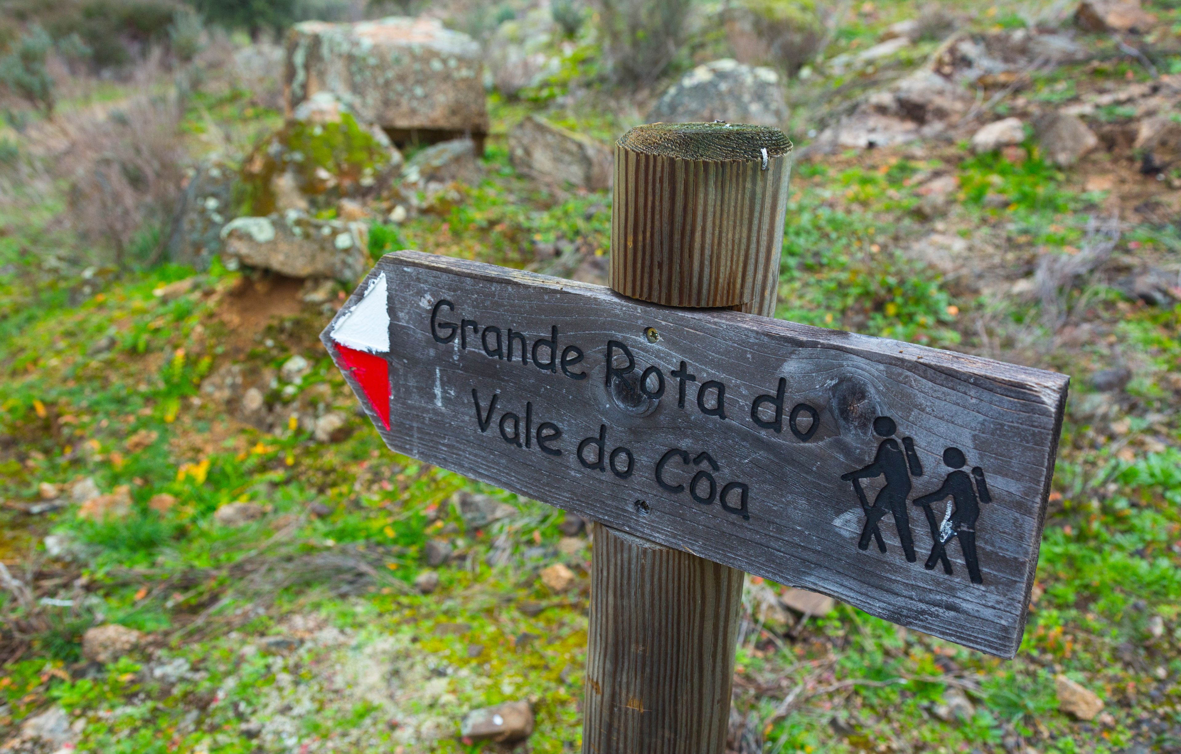 Un cartel de madera con una flecha roja apuntando a la izquierda, indicando el camino a Grande Rota do Vale do Côa.