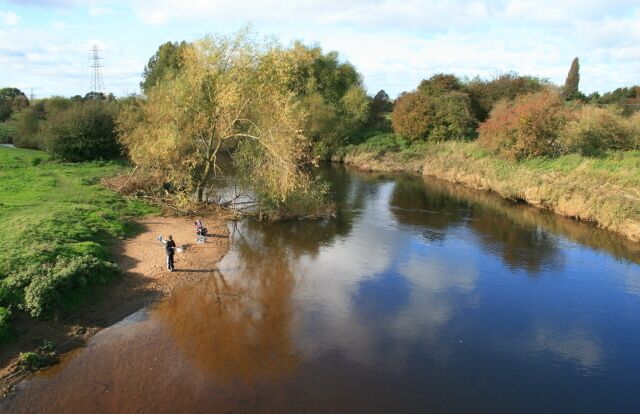 A calm river with people fishing, surrounded by trees and greenery.