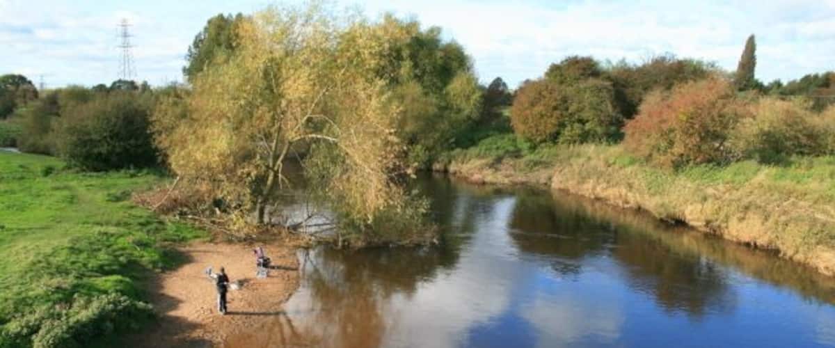 A calm river with people fishing, surrounded by trees and greenery.