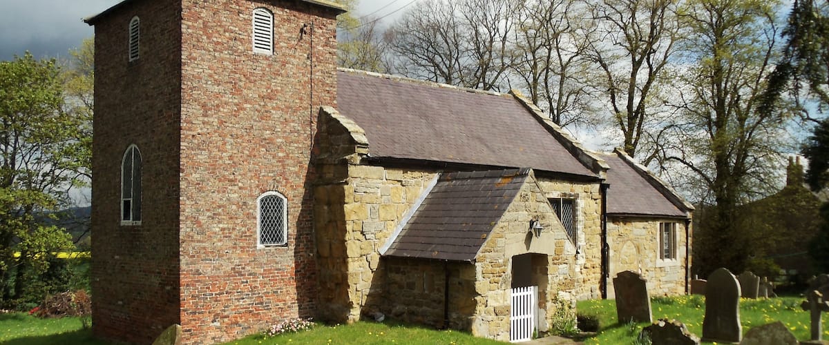 A church with a brick tower and stone walls, surrounded by a cemetery with headstones.