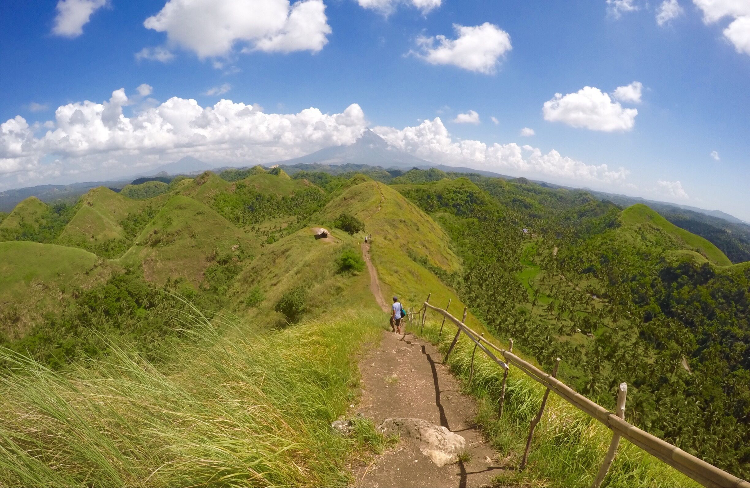 A hiking trail on a grassy hill with a wooden fence and a person walking.