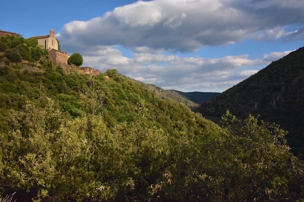 Un bâtiment historique en pierre, situé sur une colline, entouré d’une forêt verdoyante et d’une vallée.