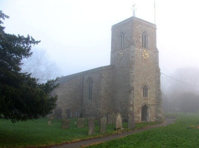 A foggy church with a clock tower and gravestones in the foreground.
