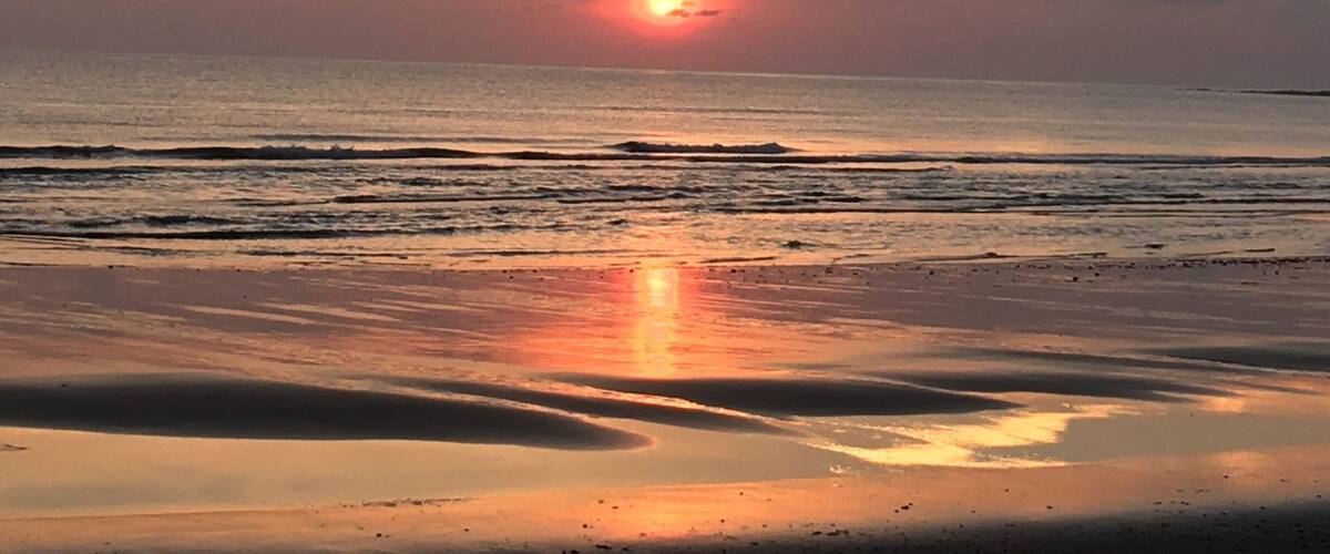 A sunset over a beach with waves and a clear sky.
