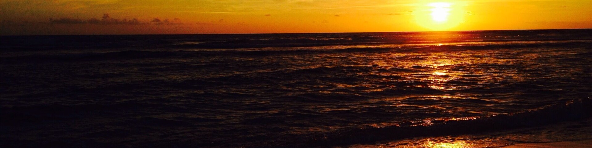 A sunset over the ocean with waves reflecting the sun's light.
