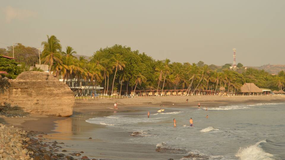 A beach with palm trees, a rocky shoreline, and a thatched-roof hut.