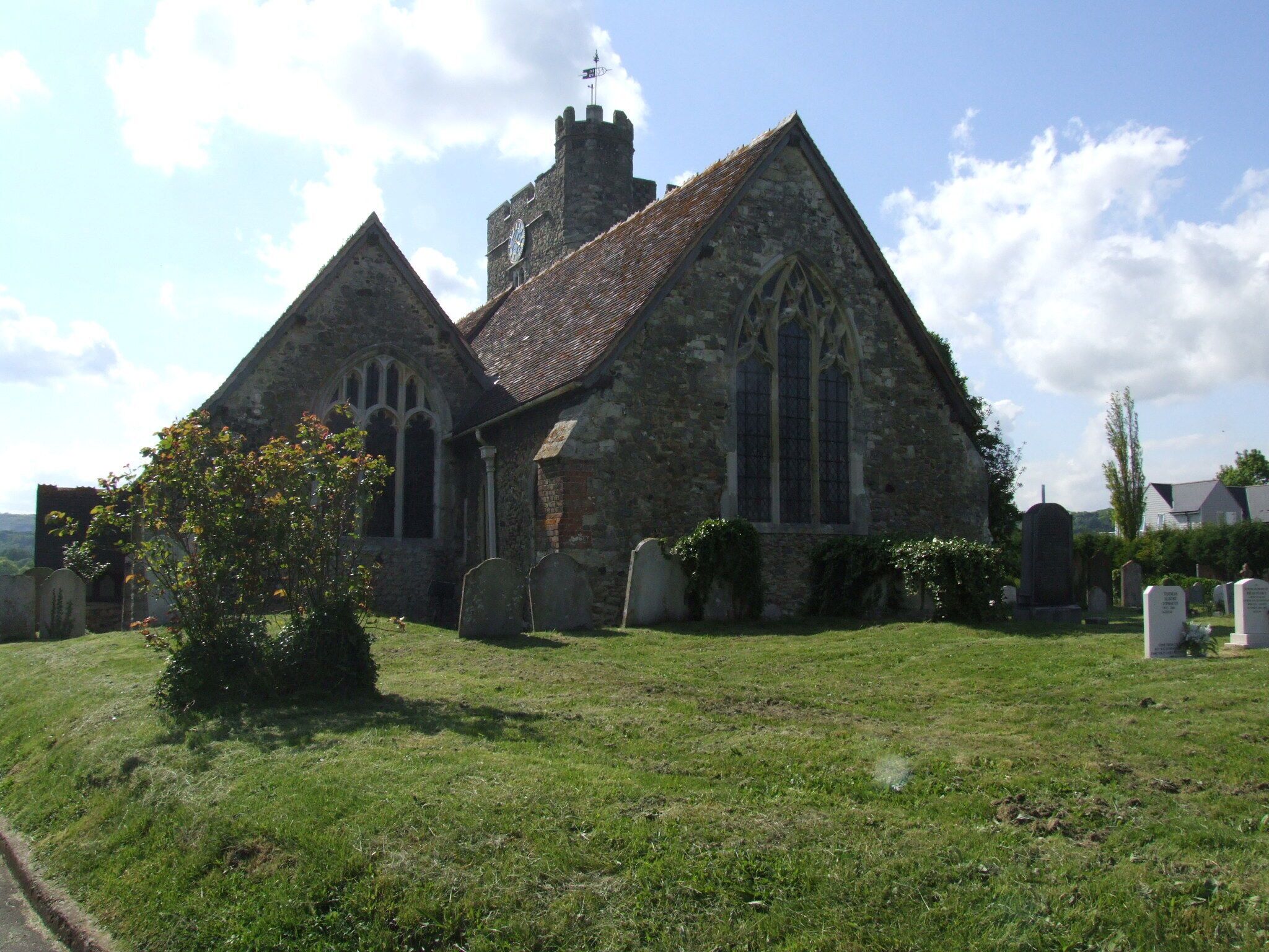 A stone church with a clock tower and a graveyard in front.