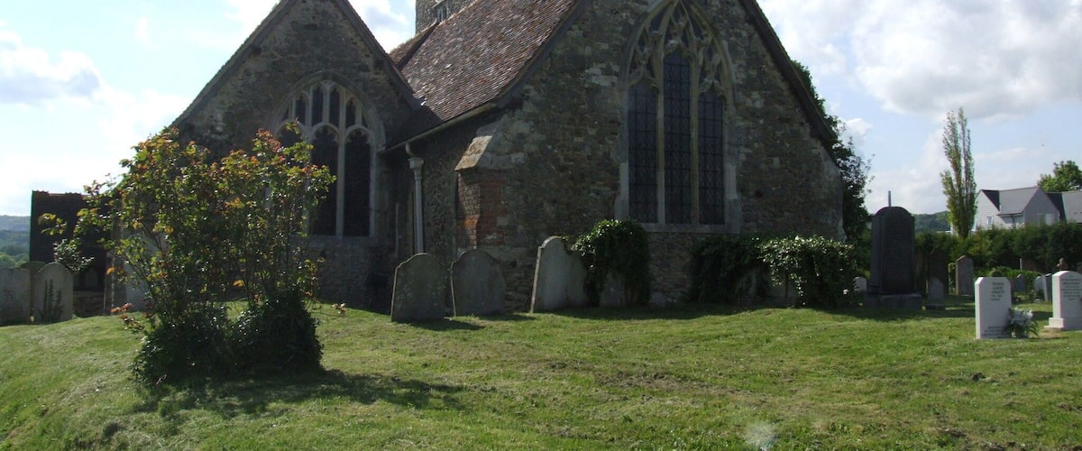 A stone church with a clock tower and a graveyard in front.