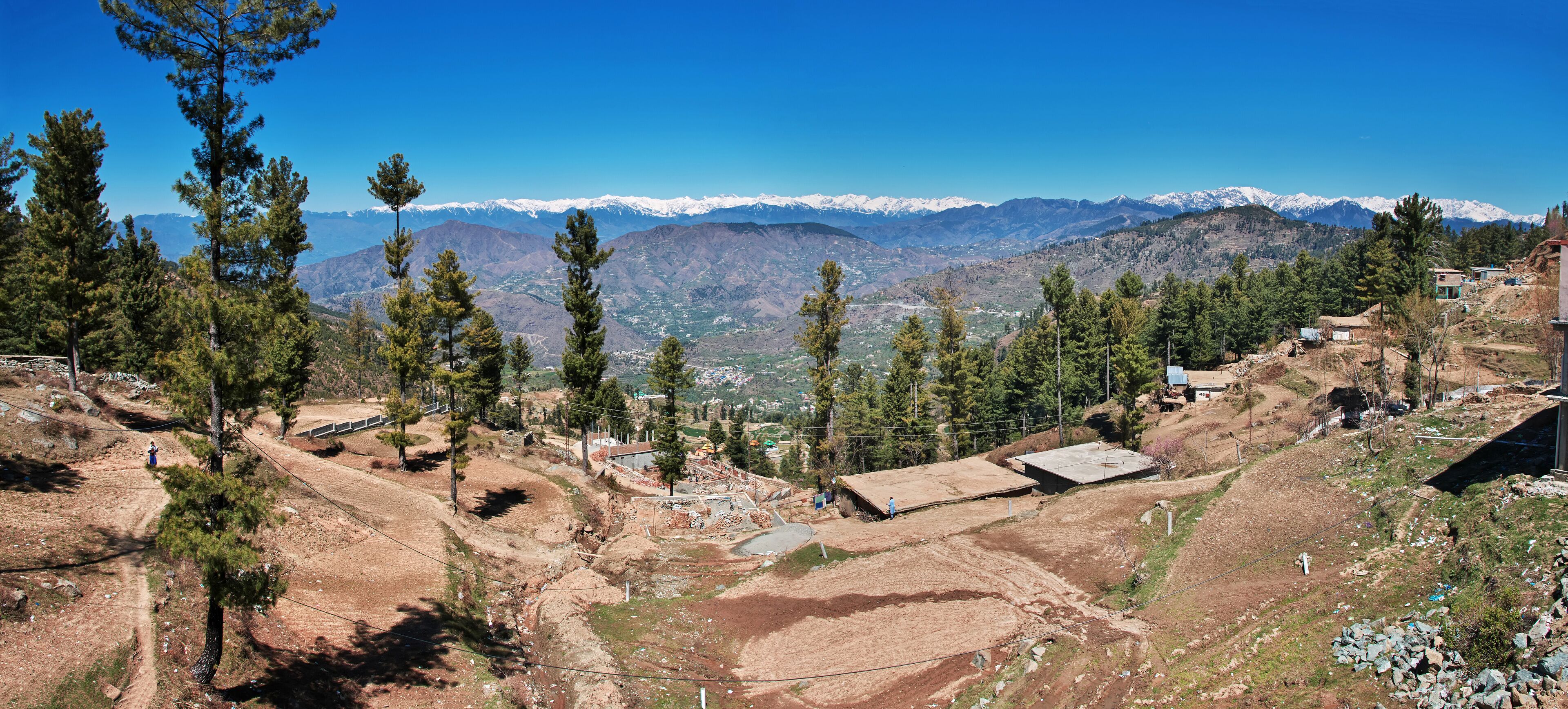 A mountainous landscape with snow-capped peaks, scattered trees, and a few buildings.