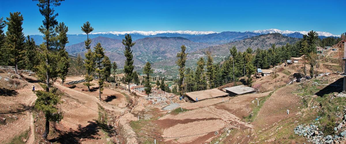 A mountainous landscape with snow-capped peaks, scattered trees, and a few buildings.