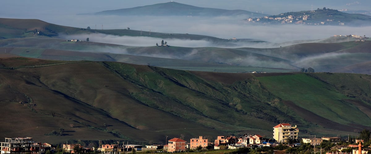 Rolling hills, a village, and a mountain in the distance.