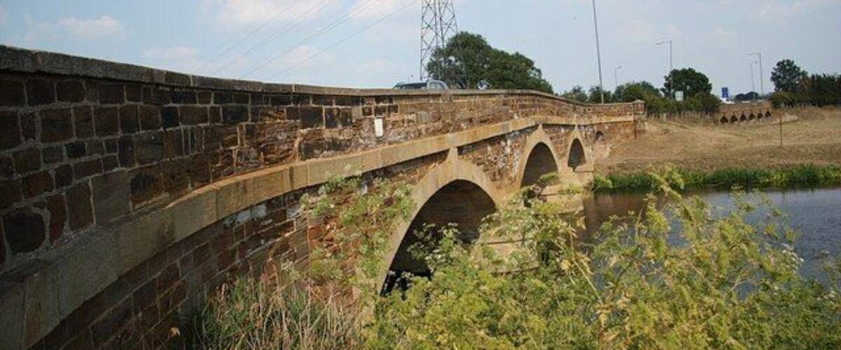 A stone bridge over a river with a power line tower in the background.
