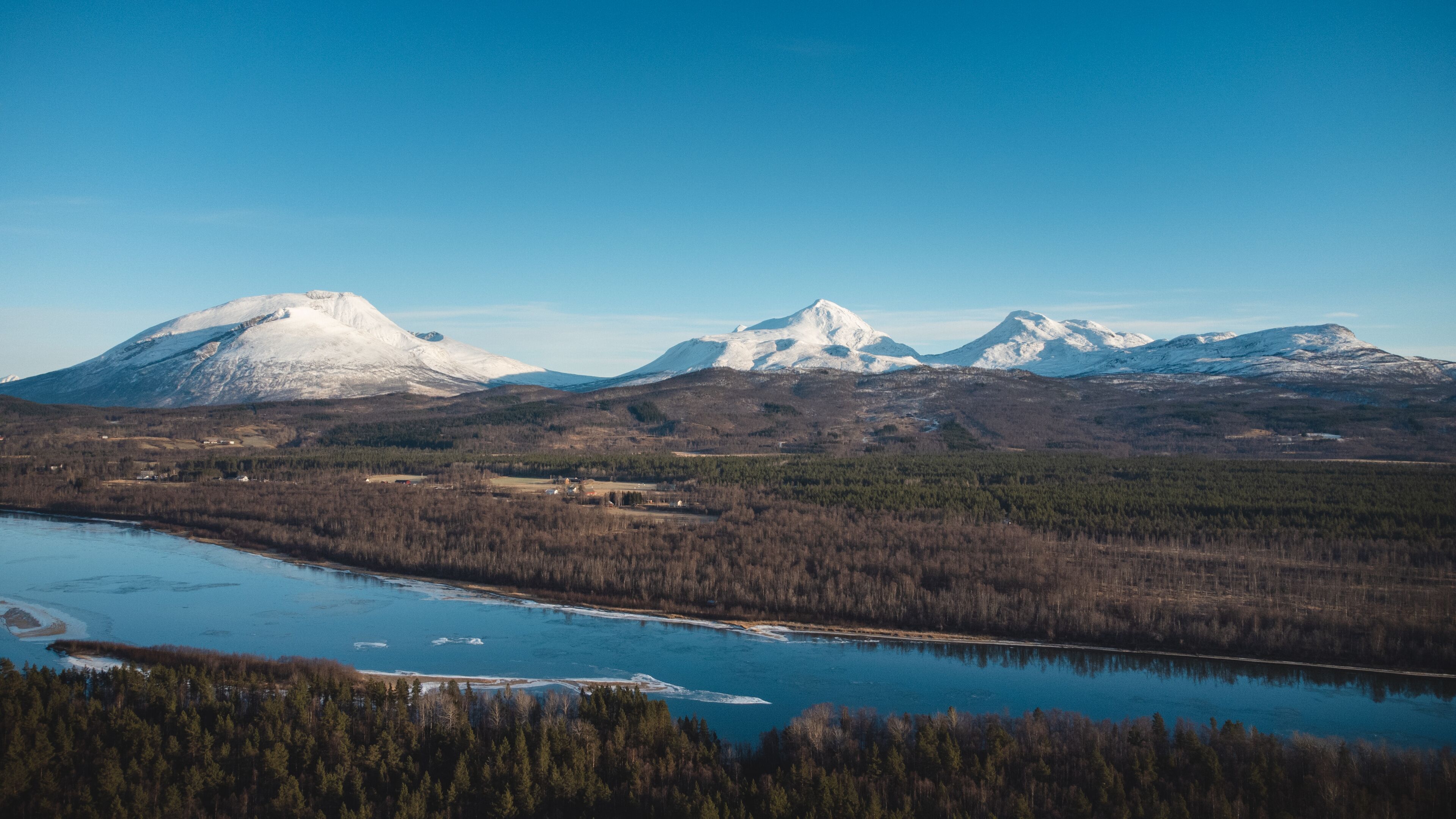 A mountain range with snow-capped peaks, a river, and a forested area.