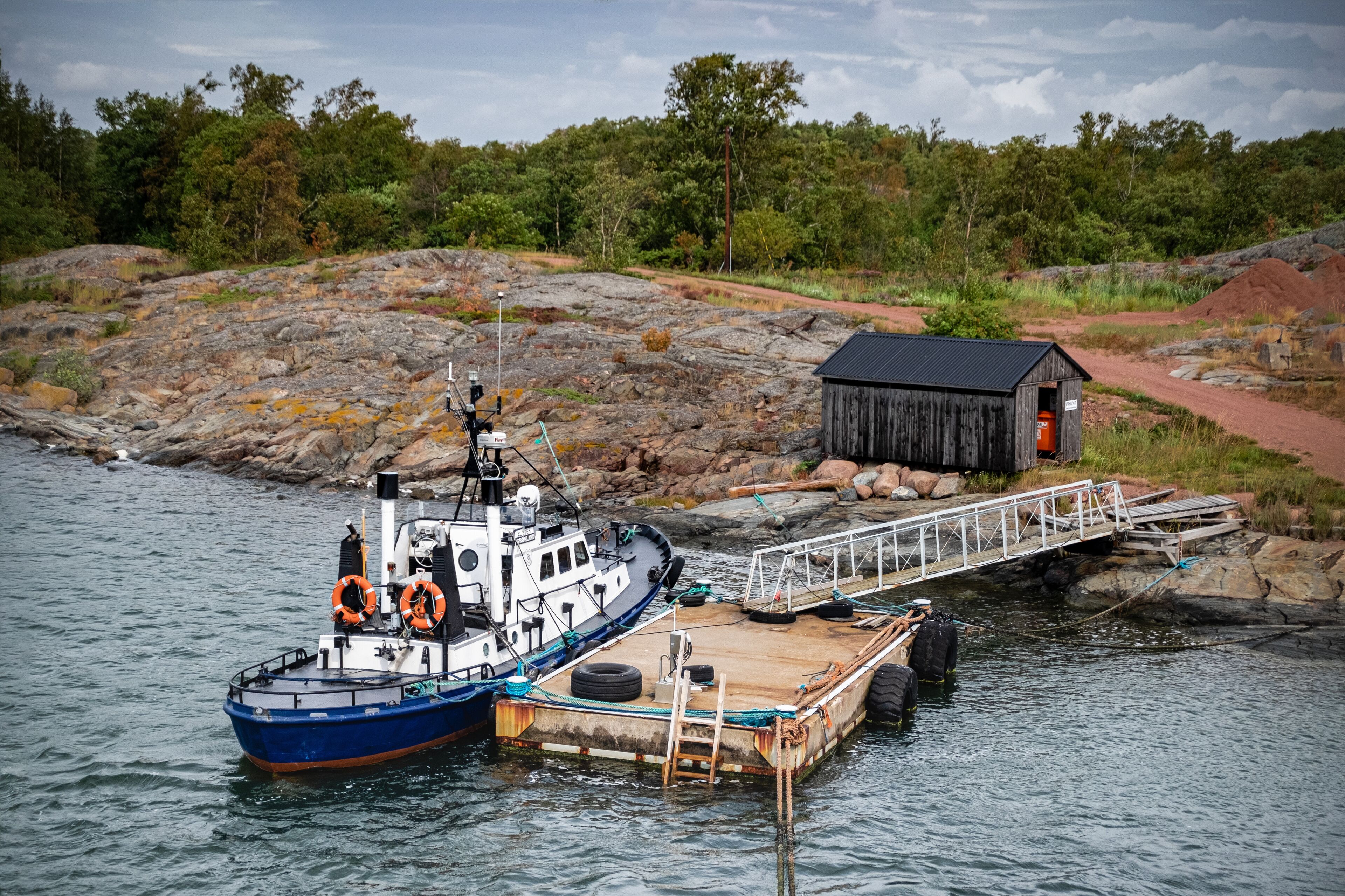 A blue and white boat docked at a wooden pier with a small shed in the background.