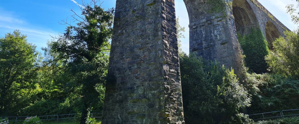 A large stone bridge with multiple arches, surrounded by lush greenery and trees.